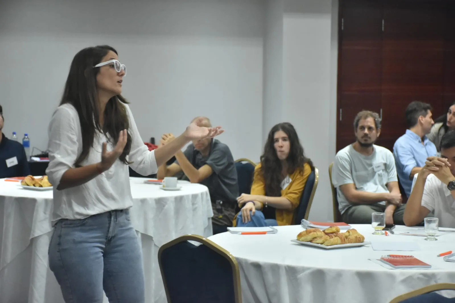 Una formadora conversa con docentes sentados en mesas redondas